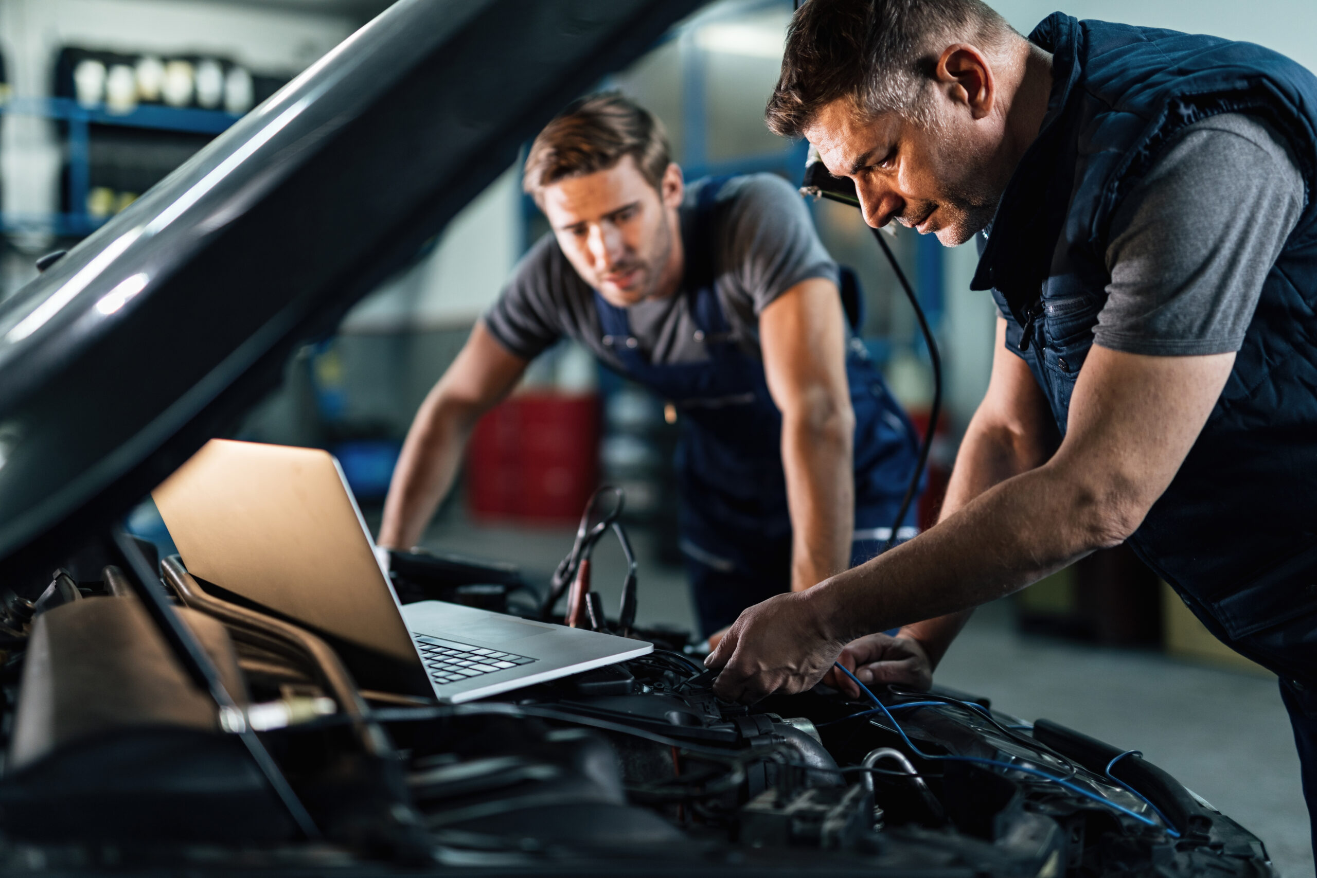 Car repairmen using laptop while doing car engine diagnostic in auto repair shop.
