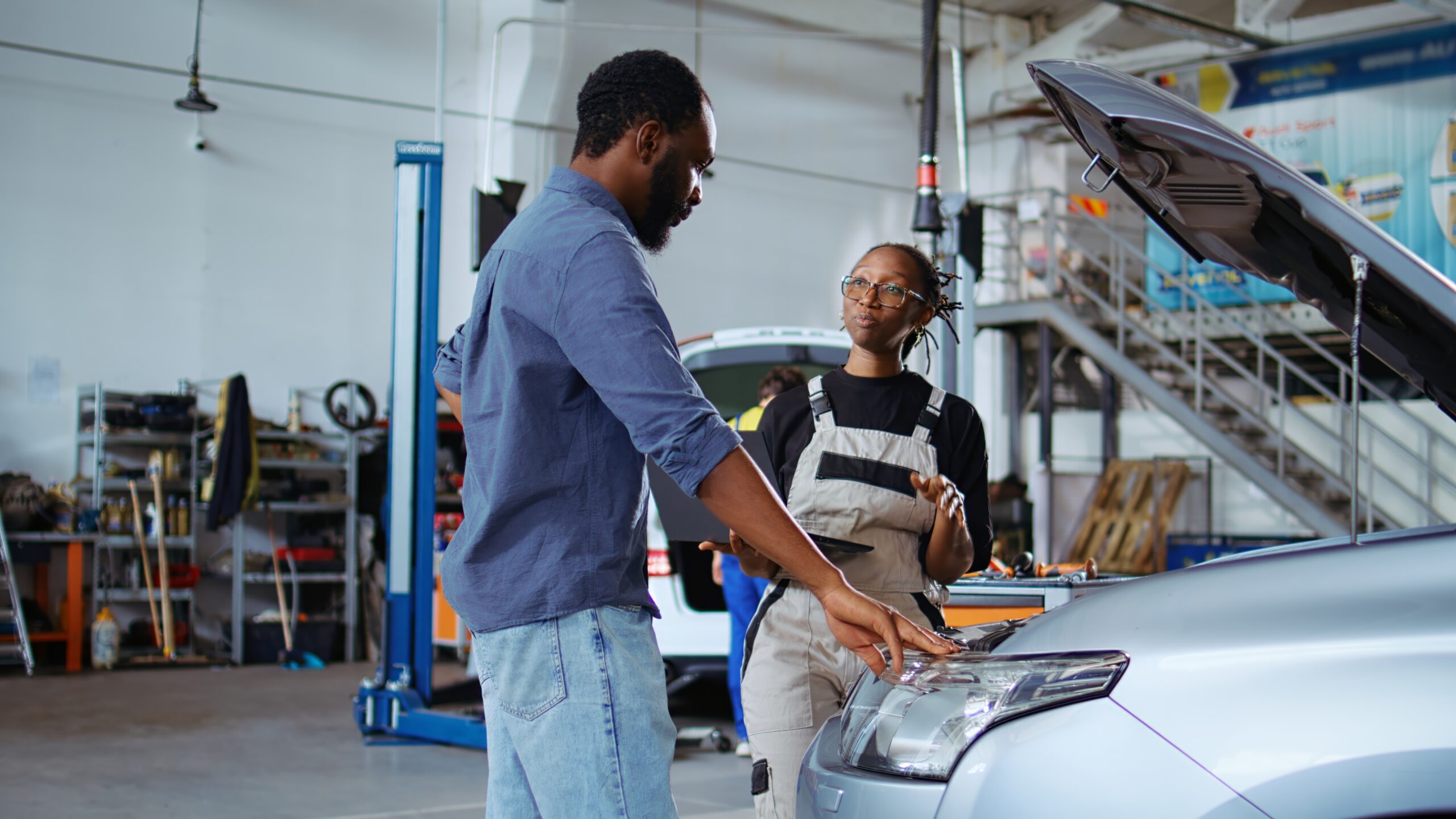 Knowledgeable employee listens to customer in repair shop, using laptop to write down car modifications needed. Worker in garage with client, listening to her requests, zoom in shot